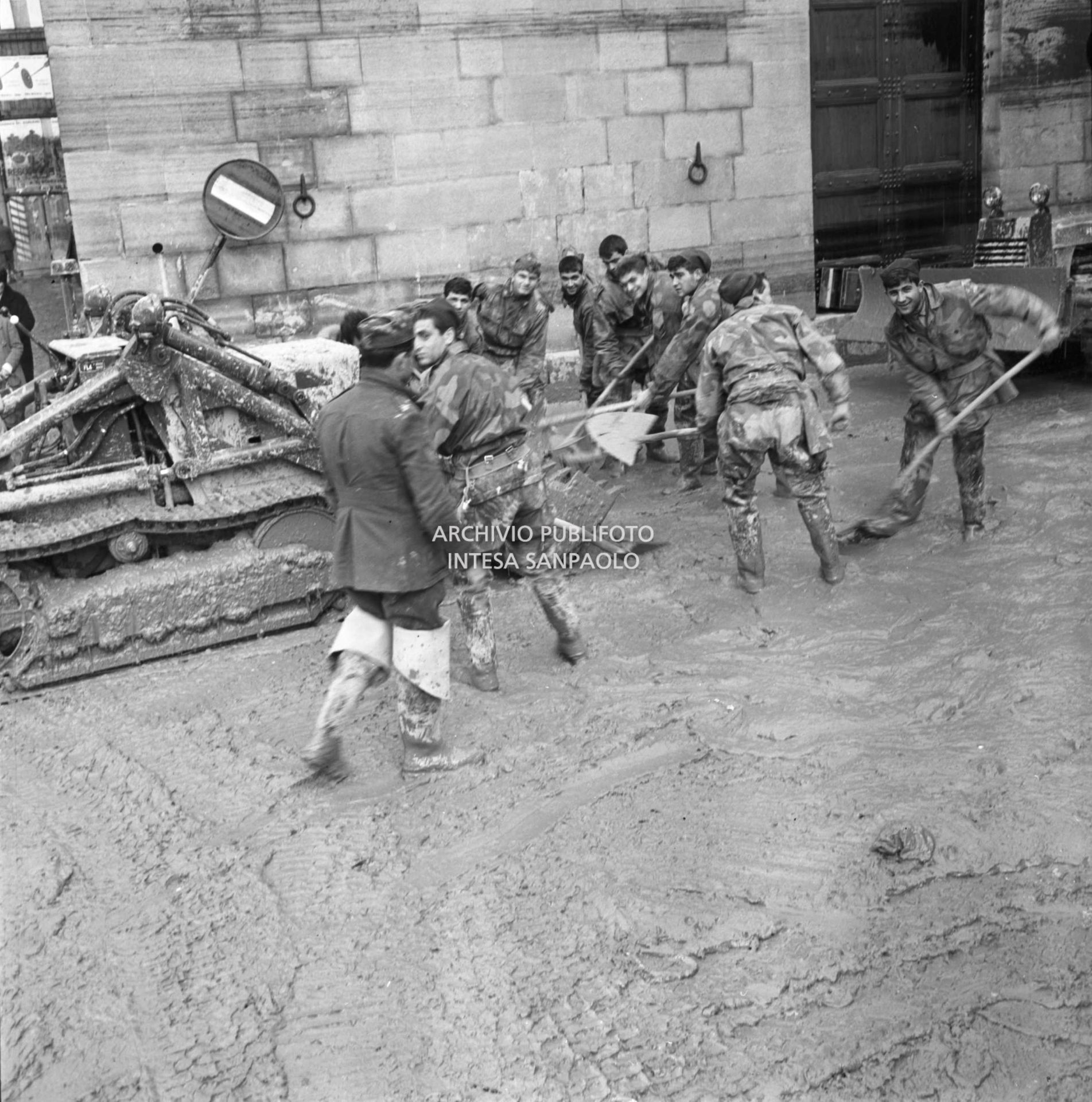 Alluvione di Firenze: militari spalano il fango in una via della città; a sinistra una ruspa cingolata