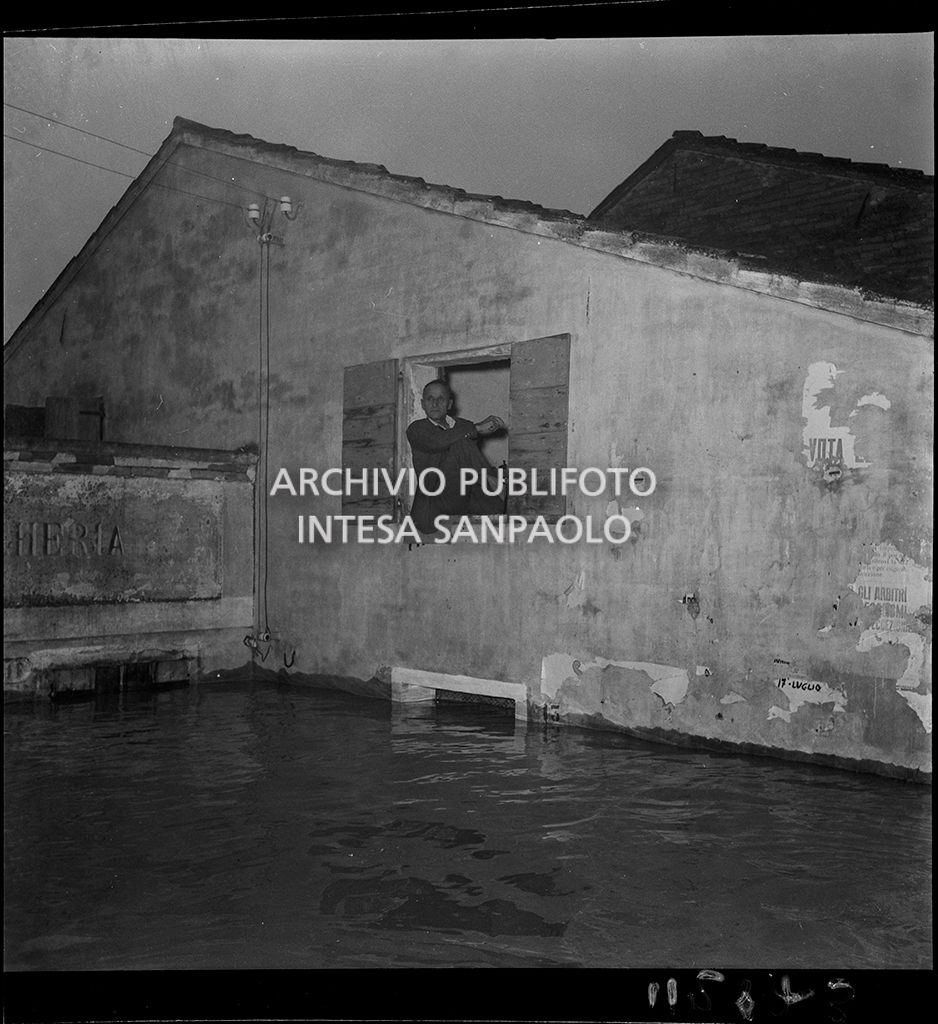 Un uomo seduto sul davanzale di una di finestra un edificio parzialmente sommerso dall'acqua durante l'alluvione del Polesine