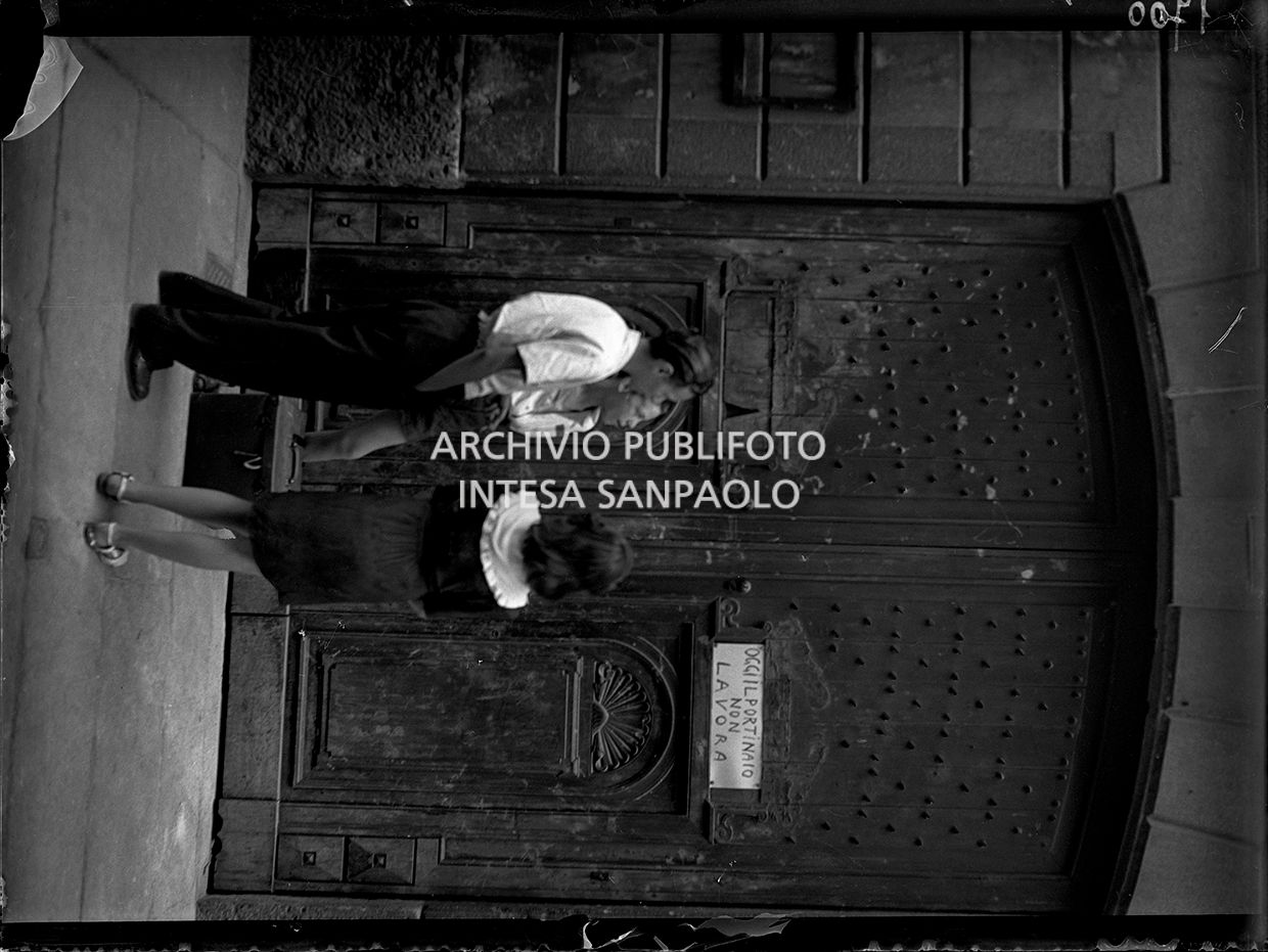 Ragazzini davanti a un portone chiuso a causa dello sciopero dei portinai. Sul portone il cartello: "Oggi il portinaio non lavora"