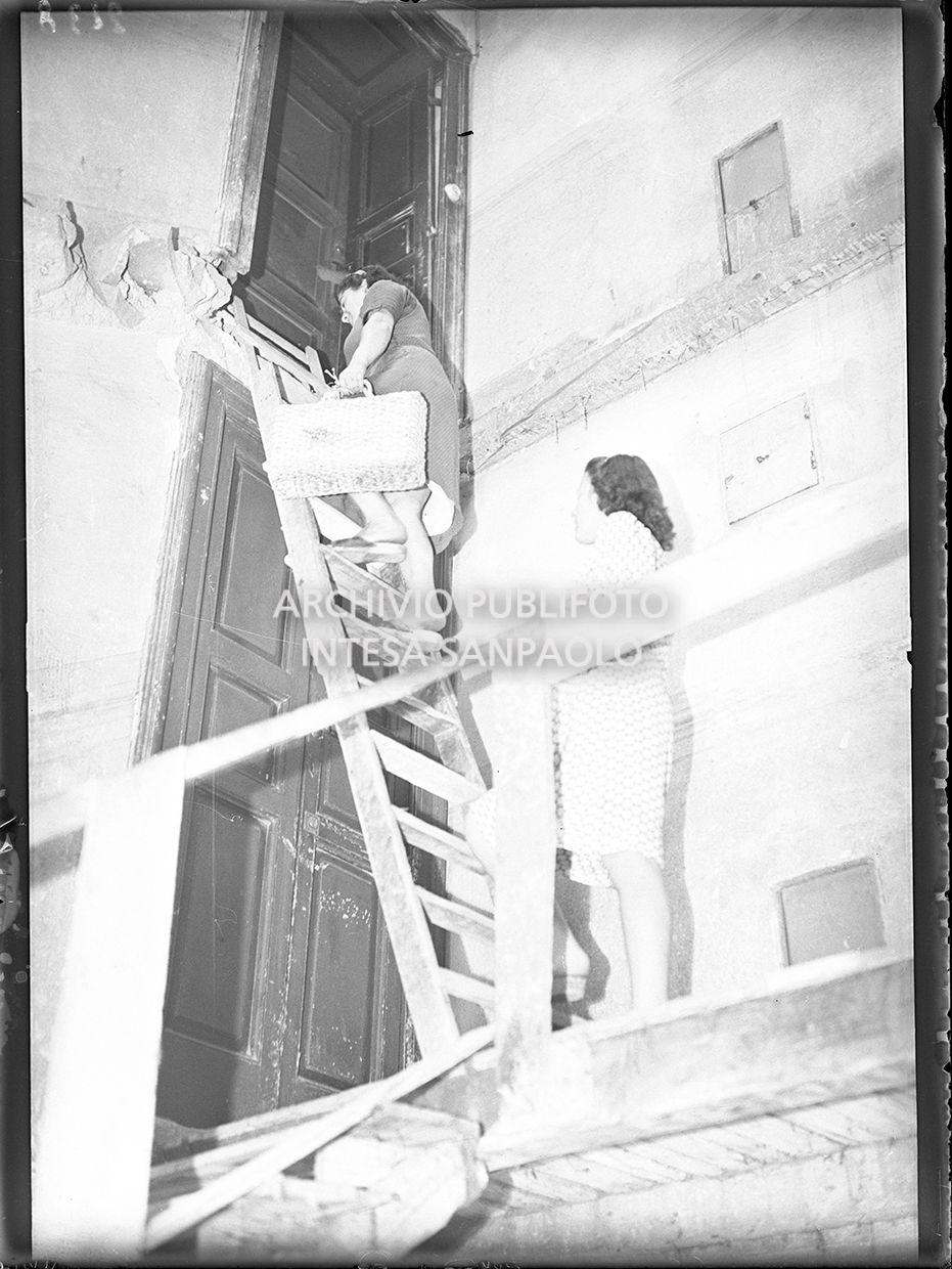 Una donna accede alla sua abitazione, in uno stabile danneggiato dai bombardamenti, con una scala a pioli
