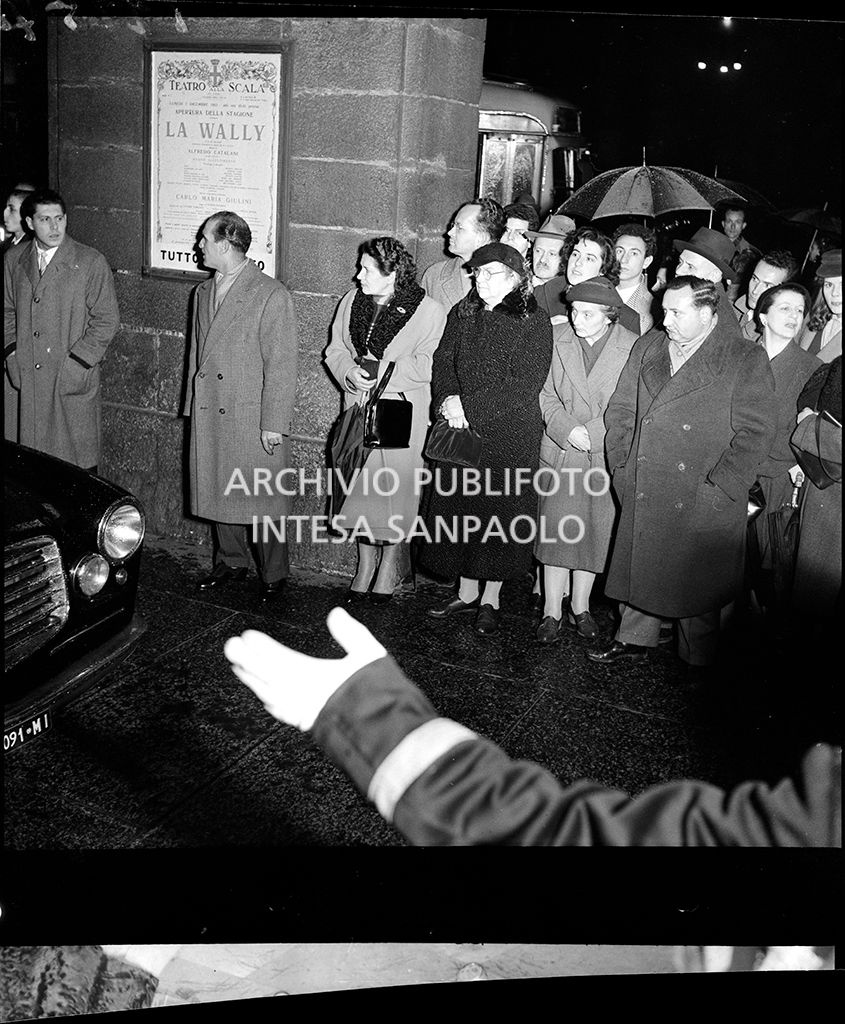 Spettatori in attesa delle automobili nella galleria delle carrozze del Teatro alla Scala in occasione della serata inaugurale della stagione lirica 1953-1954 con l'opera "La Wally", di Alfredo Catalani, diretta da Carlo Maria Giulini, con la regia di Tatiana Pavlova
