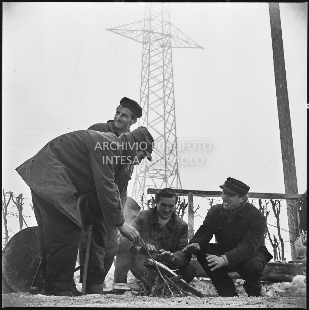 Operai si riscaldano davanti ad un fuoco durante i lavori per l'allacciamento dei cavi elettrici della Edison<br>196179