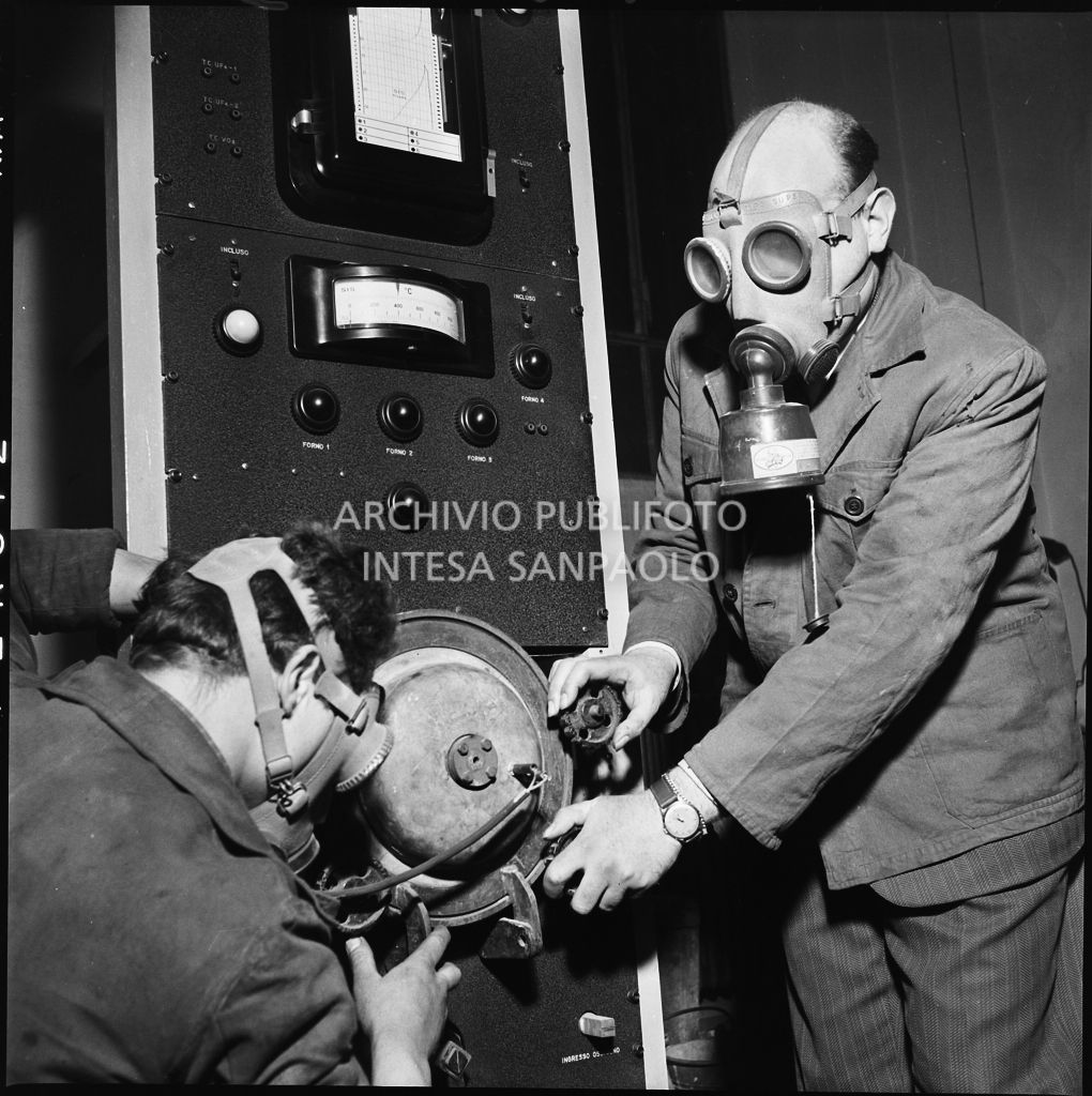 Due uomini con maschera anti gas al lavoro su un impianto del CISE<br>196219