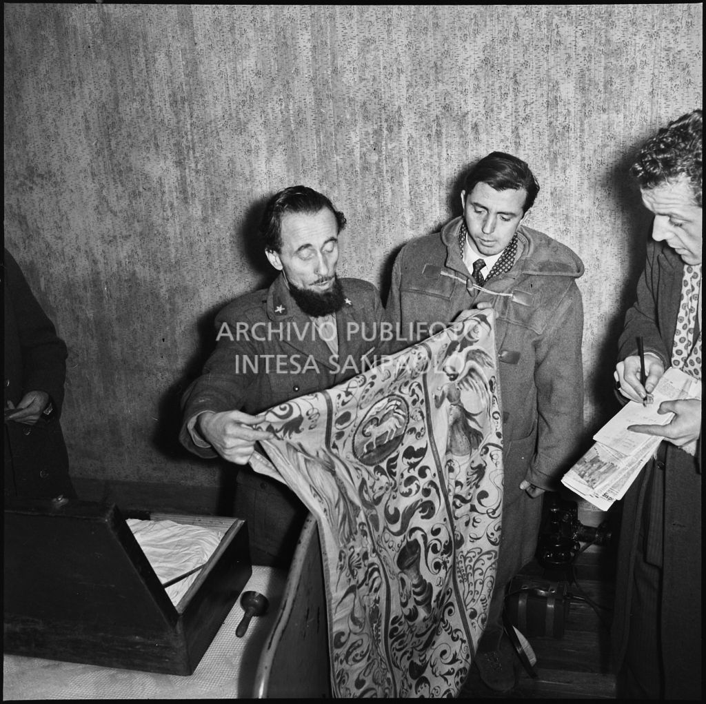 Padre Brevi, circondato da giornalisti, mostra alcuni oggetti religiosi al rientro in patria dopo la prigionia in Unione Sovietica<br>196379