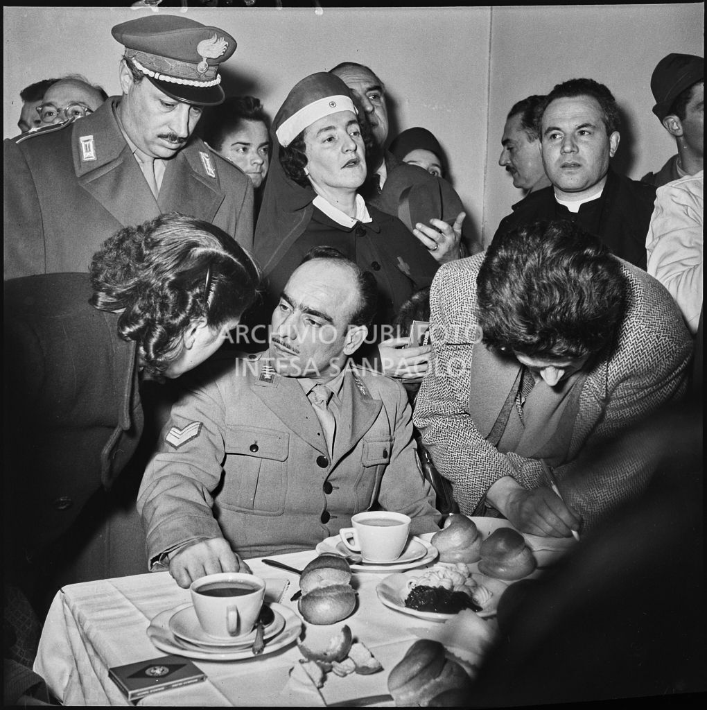 Un ex prigioniero italiano di rientro dall'Unione Sovietica fa colazione circondato da un giornalista e persone in festa<br>196497