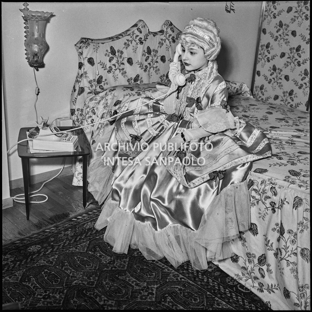 Una bambina con un costume da carnevale ritratta mentre parla al telefono<br>201830