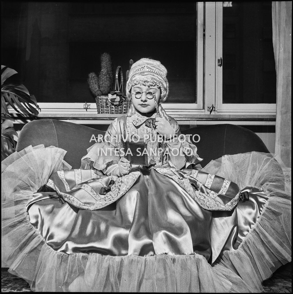 Una bambina con un costume da carnevale finge di leggere un libro<br>201835