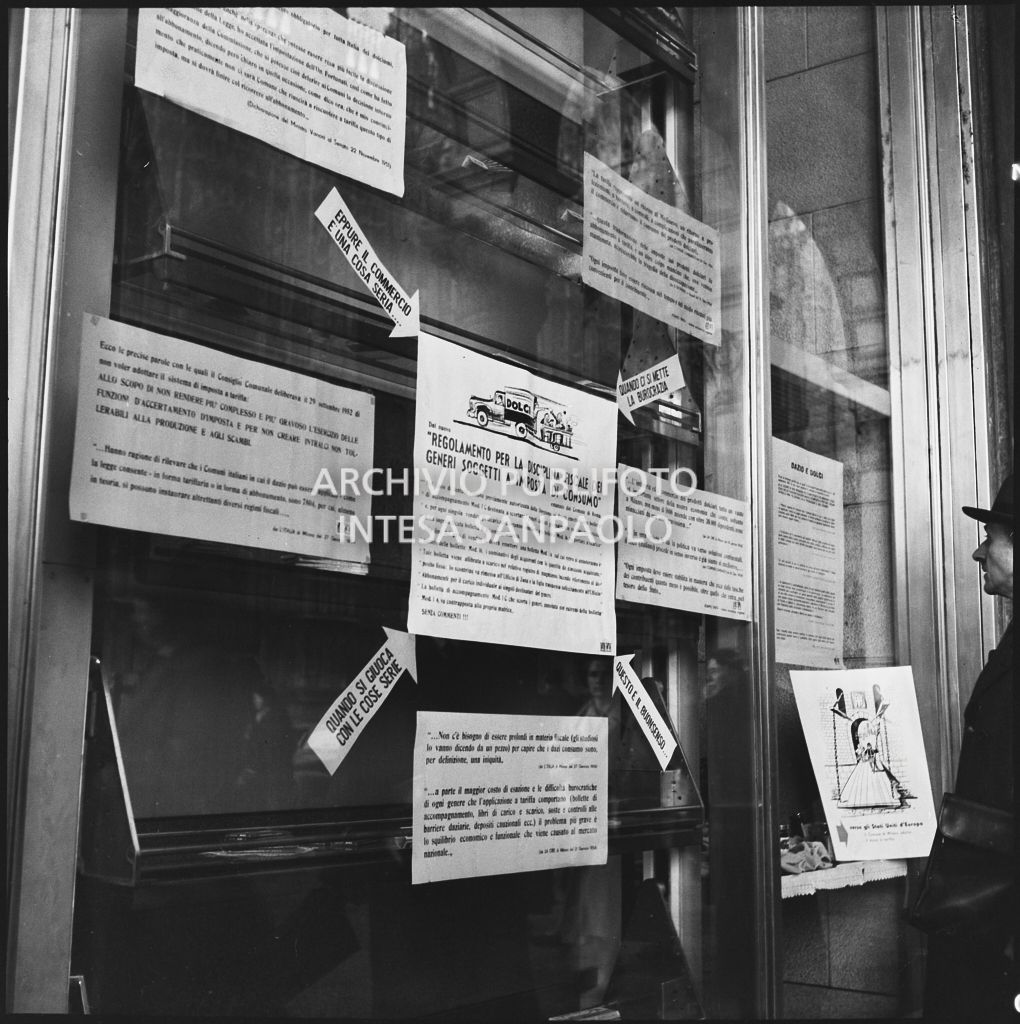 Vetrina del negozio Motta nella Galleria Vittorio Emanuele II a Milano con i manifesti del "Regolamento per la disciplina fiscale dei generi soggetti a imposta di consumo"<br>201850