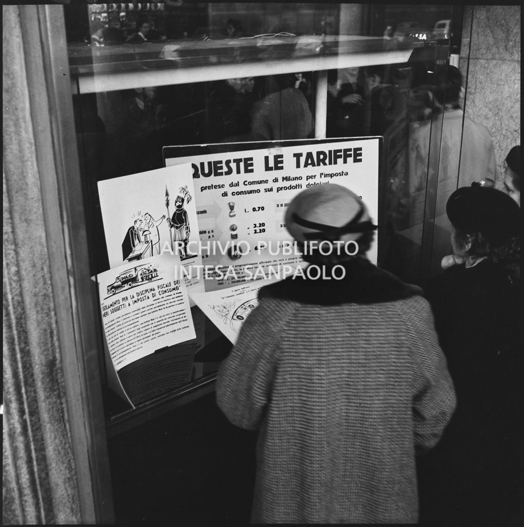 Una signora consulta le tariffe imposte dal "Regolamento per la disciplina fiscale dei generi soggetti a imposta di consumo" esposte in una vetrina del negozio Motta nella Galleria Vittorio Emanuele II a Milano<br>201852