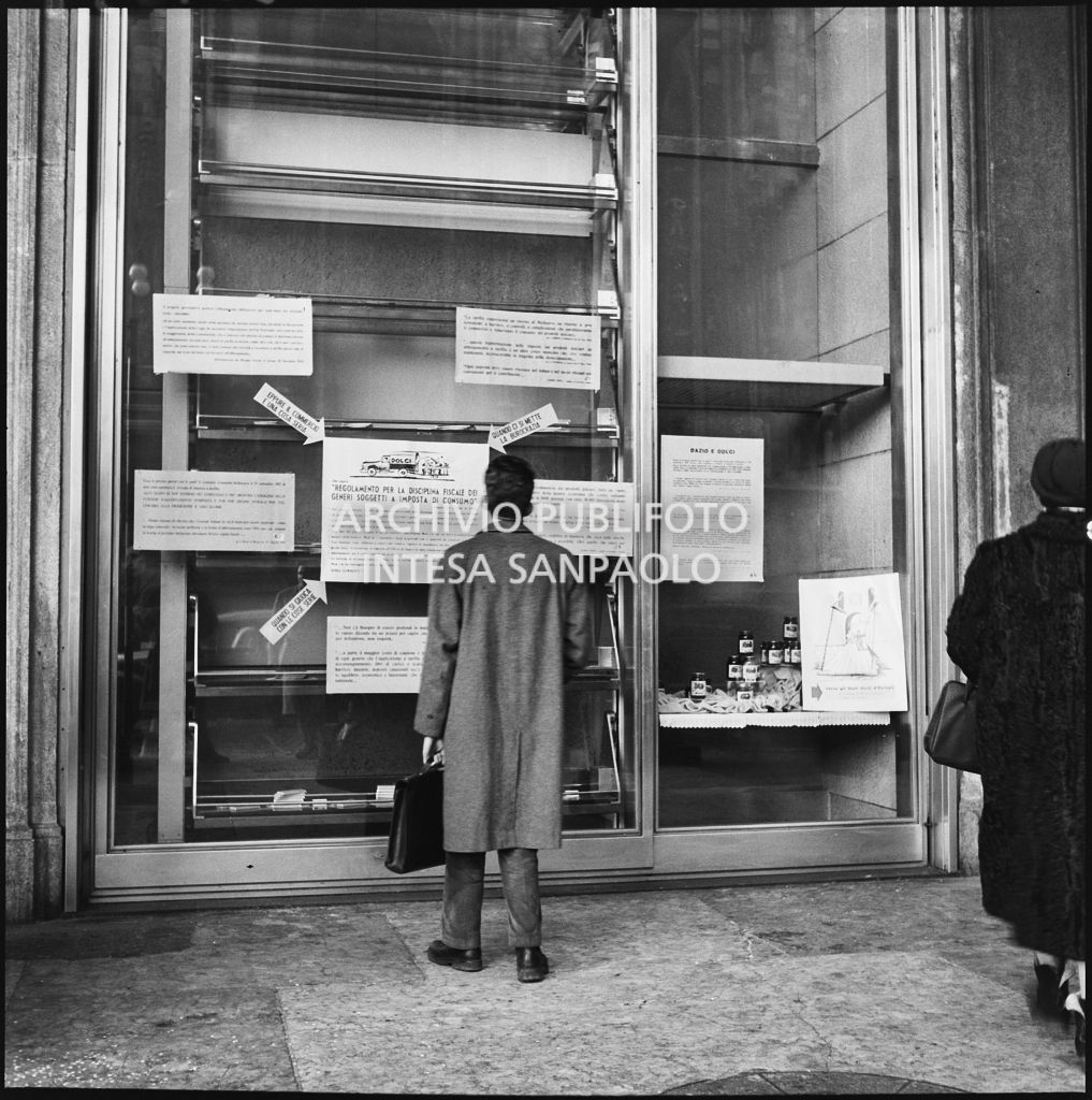 Vetrina del negozio Motta nella Galleria Vittorio Emanuele II a Milano con i manifesti del "Regolamento per la disciplina fiscale dei generi soggetti a imposta di consumo"<br>201853