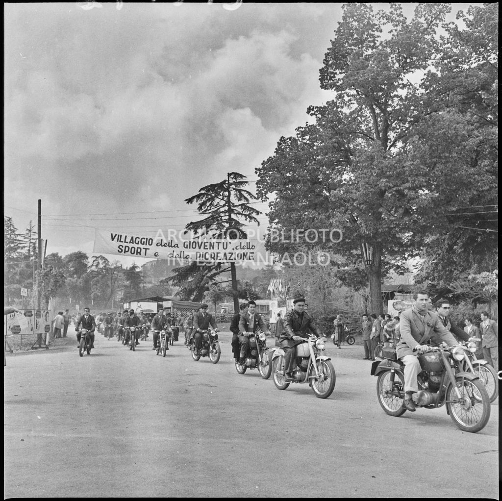 Un gruppo di uomini in moto, uno striscione appeso recita: Villaggio della gioventù, dello sport e della ricreazione<br>212196