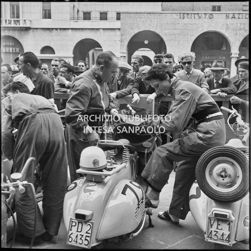 Concorrenti in un momento di pausa dalla competizione sportiva 1000 Km Vespistica del 1954 in piazza della Vittoria a Brescia<br>216183