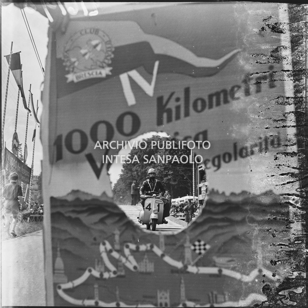 Partenza del concorrente Emilio Gasparotto del Vespa Club di Vicenza (numero di gara 41) per la competizione sportiva 1000 Km Vespistica del 1954 visto attraverso il cartellone della gara<br>216198