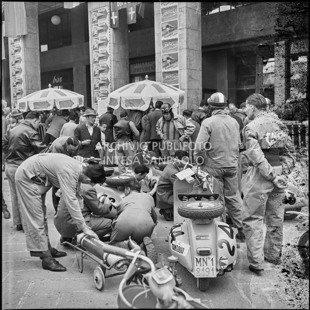 Scrittura del numero di gara sugli scooter Vespa dei concorrenti della competizione sportiva 1000 Km Vespistica del 1954 in piazza della Vittoria a Brescia<br>216221