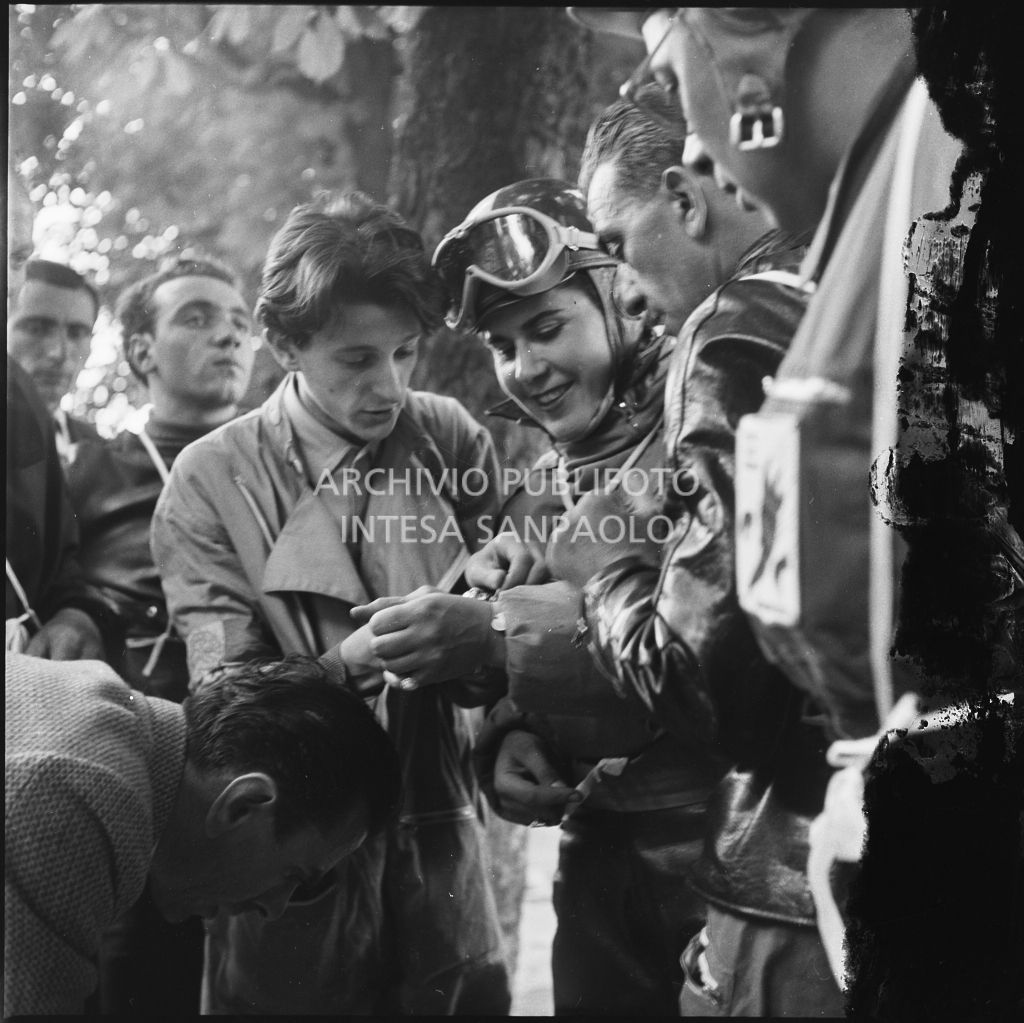 La concorrente Ada Pace del Vespa Club di Torino (numero di gara 1) circondata da altri concorrenti della competizione sportiva 1000 Km Vespistica del 1954<br>216300