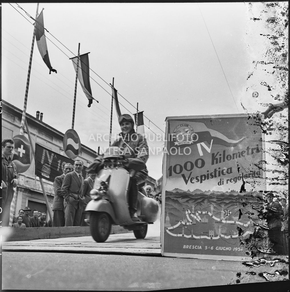 Partenza della concorrente Ada Pace del Vespa Club di Torino (numero di tra 1) per la competizione sportiva 1000 Km Vespistica del 1954. Visibile in primo piano il cartellone della gara<br>216310