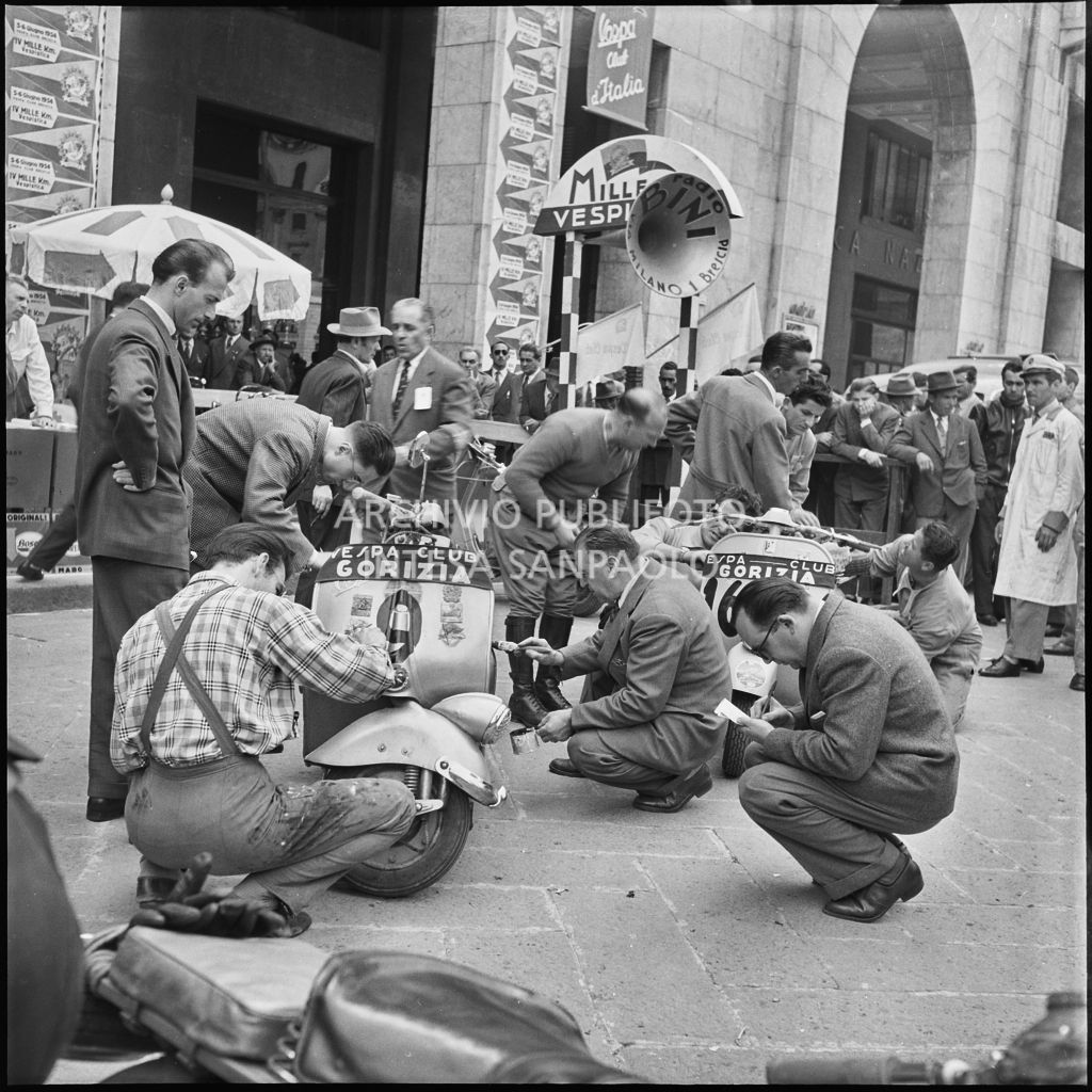 Scrittura del numero di gara sugli scooter Vespa dei concorrenti della competizione sportiva 1000 Km Vespistica del 1954 in piazza della Vittoria a Brescia<br>216316