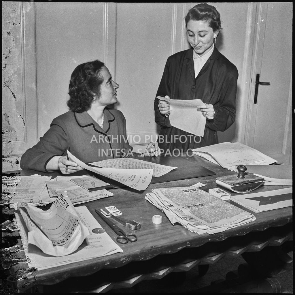 Due donne alla scrivania in occasione del convegno di studio sulle condizioni del lavoratore nell'impresa industriale organizzata nei Chiostri di San Barnaba a Milano dalla Società Umanitaria. Sulla scrivania una busta da lettere della Publifoto<br>216347