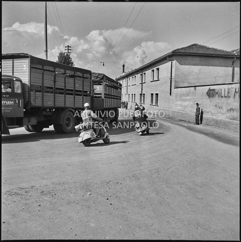 Alcuni concorrenti della competizione sportiva 1000 Km Vespistica del 1954 incrociano un autocarro lungo il percorso<br>216366