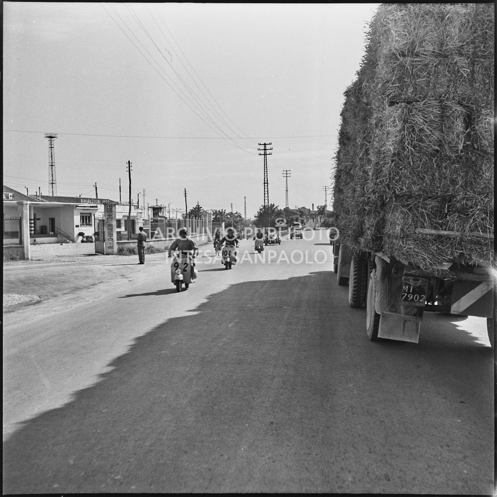 Alcuni concorrenti della competizione sportiva 1000 Km Vespistica del 1954 incontrano un autocarro ricolmo di fieno lungo il percorso<br>216379