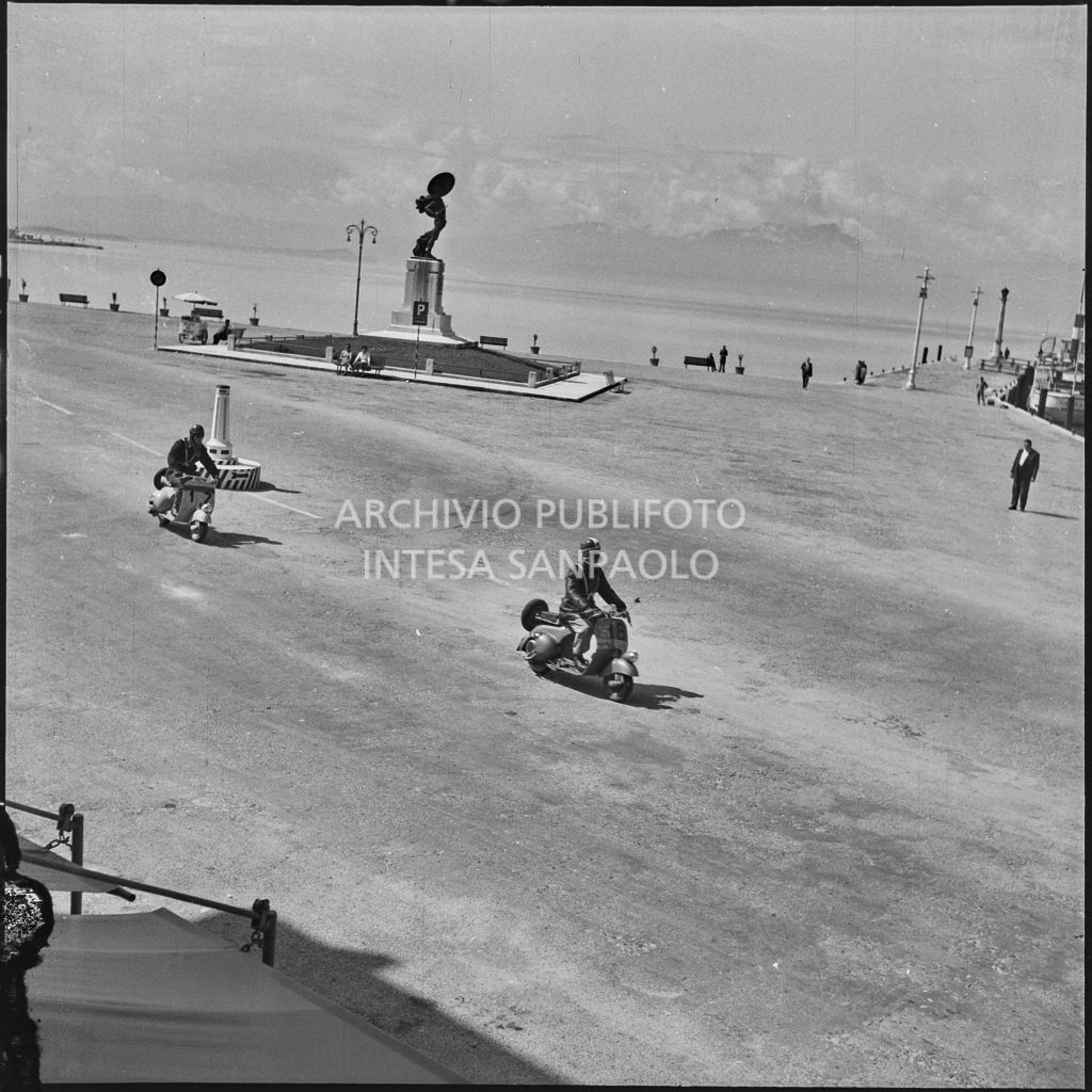 Il concorrente Bruno Camplani del Vespa Club di Lecco (numero di gara 18) e un altro concorrente (numero di gara 17) a Peschiera del Garda durante la competizione sportiva 1000 Km Vespistica del 1954<br>216416