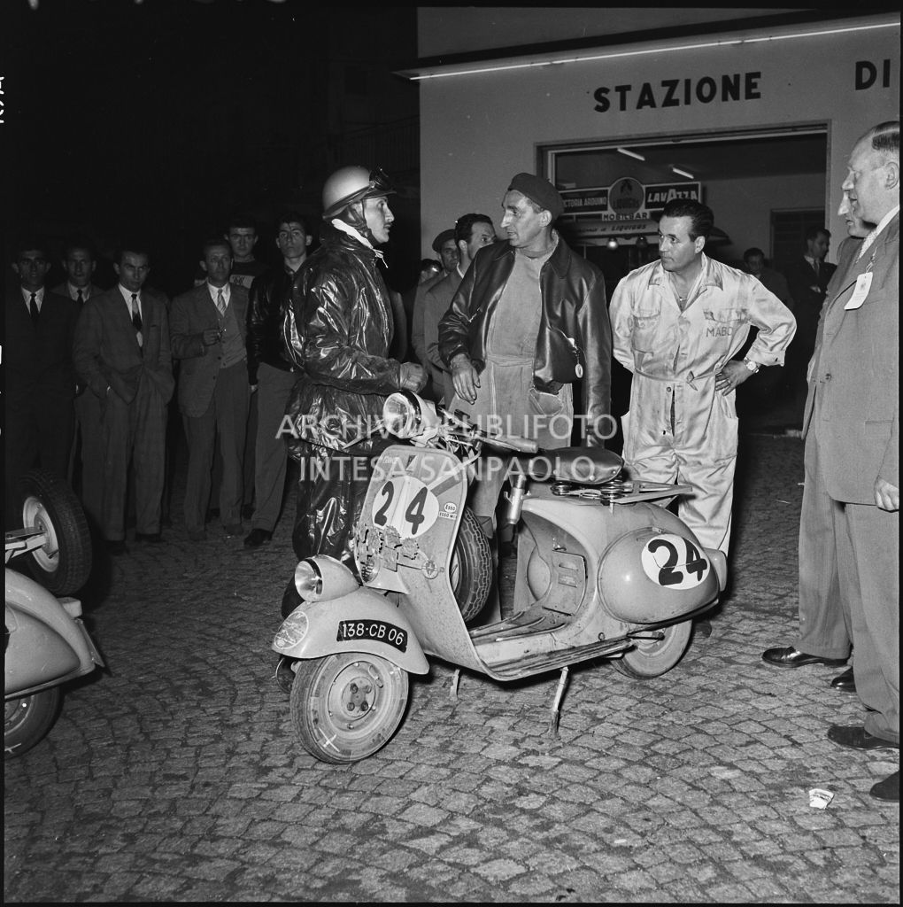 Il concorrente Rudy Aragno del Vespa Club di Parigi (numero di gara 24) della competizione sportiva 1000 Km Vespistica del 1954 durante una pausa rifornimento<br>216434