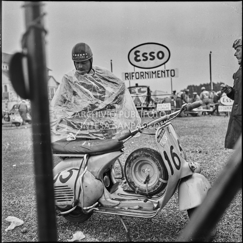 Un concorrente (numero di gara 165) con un impermeabile in un momento di pausa dalla competizione sportiva 1000 Km Vespistica del 1954<br>216465