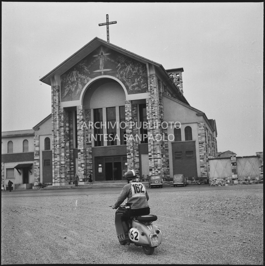 Un concorrente (numero di gara 162) nei pressi di una chiesa durante una pausa dalla competizione sportiva 1000 Km Vespistica del 1954<br>216474