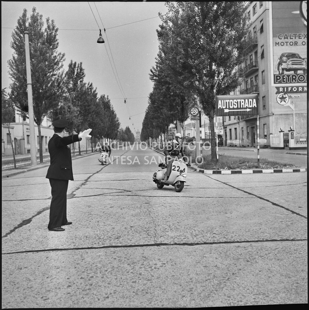 Un vigile urbano blocca il traffico per il passaggio dei concorrenti della competizione sportiva 1000 Km Vespistica del 1954<br>216480