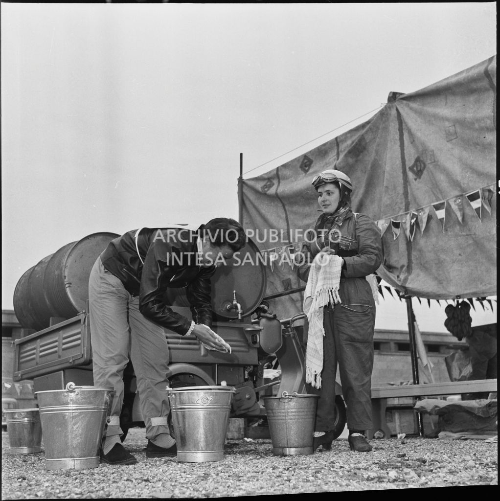 Una concorrente del Vespa Club di Venezia ed un altro concorrente si lavano le mani in un momento di pausa dalla competizione sportiva 1000 Km Vespistica del 1954<br>216484