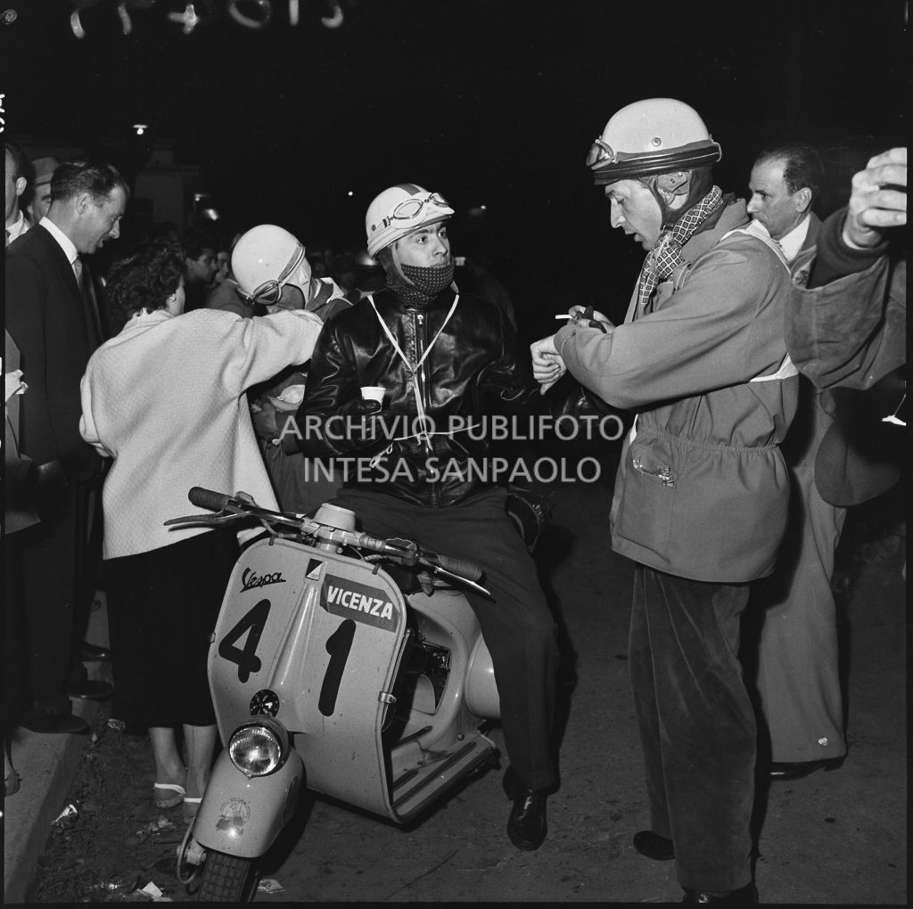 Il concorrente Emilio Gasparotto del Vespa Club di Vicenza (numero di gara 41) beve un caffè a bordo del suo scooter durante una pausa dalla competizione sportiva 1000 Km Vespistica del 1954<br>216499
