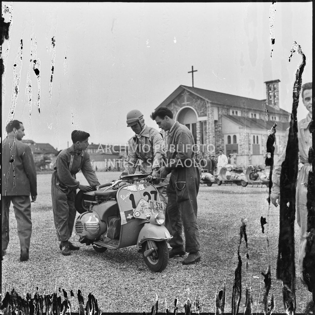Controllo della Vespa di un concorrente svizzero da parte di alcuni meccanici durante una pausa dalla competizione sportiva 1000 Km Vespistica del 1954<br>216520