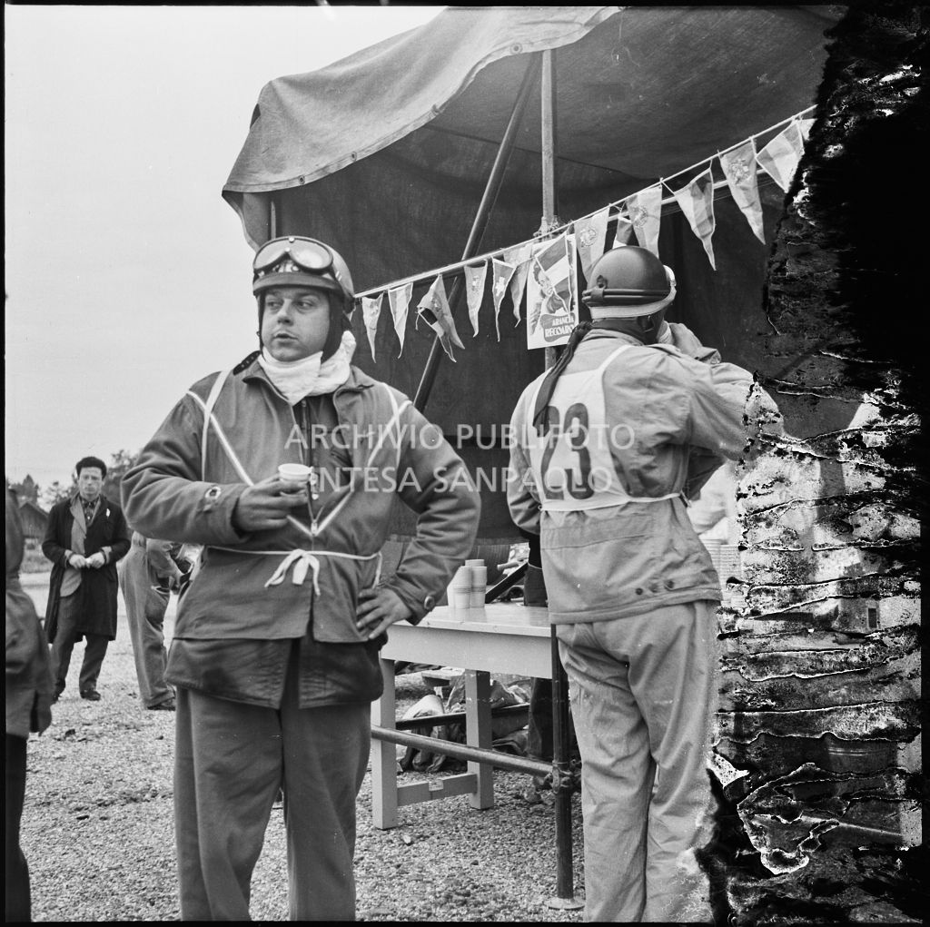 Il concorrente Giovanni mariani del Vespa Club di Brescia (numero di gara 23) ed un altro concorrente al punto ristoro durante una pausa dalla competizione sportiva 1000 Km Vespistica del 1954<br>216549