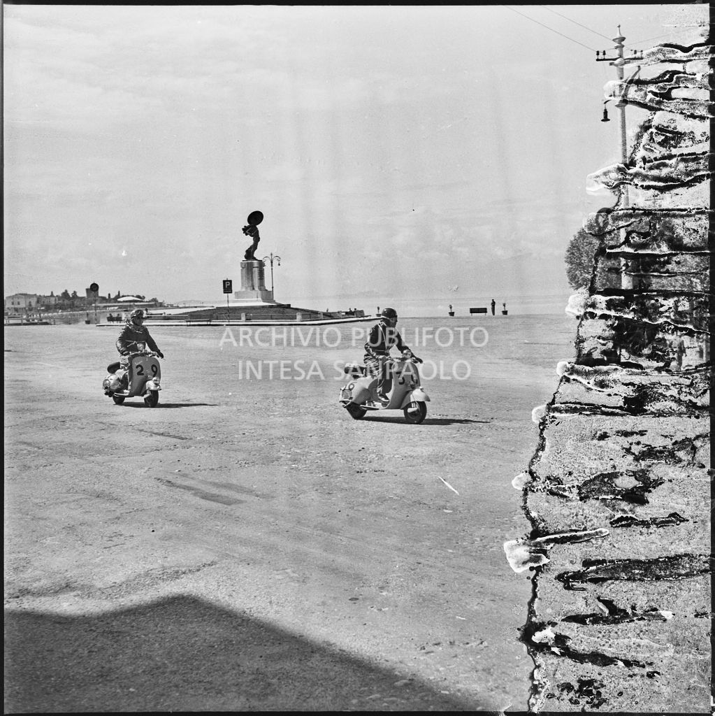 Il concorrente Osvaldo Buffarini del Vespa Club di Forlì (numero di gara 36) e il concorrente Scmaaf del Vespa Club di Dusseldorf (numero di gara 29) a Peschiera del Garda durante la competizione sportiva 1000 Km Vespistica del 1954<br>216560