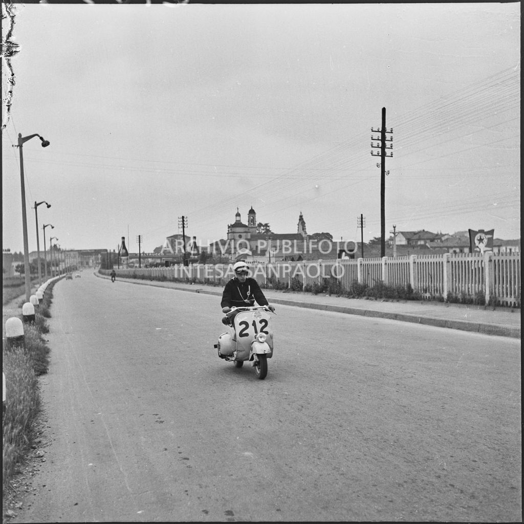 Un concorrente a Milano durante la competizione sportiva 1000 Km Vespistica del 1954. Visibile in lontananza la Certosa di Milano<br>216598
