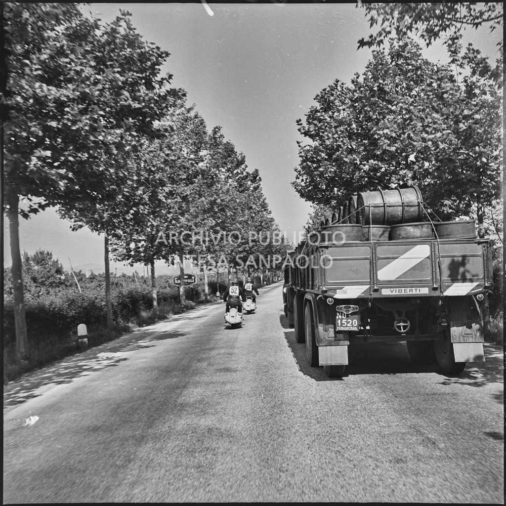 I concorrenti del Vespa Club di Chiari Benito Pagani (numero di gara 52) e Mario Pagani (numero di gara 56) superano un autocarro durante la competizione sportiva 1000 Km Vespistica del 1954<br>216609