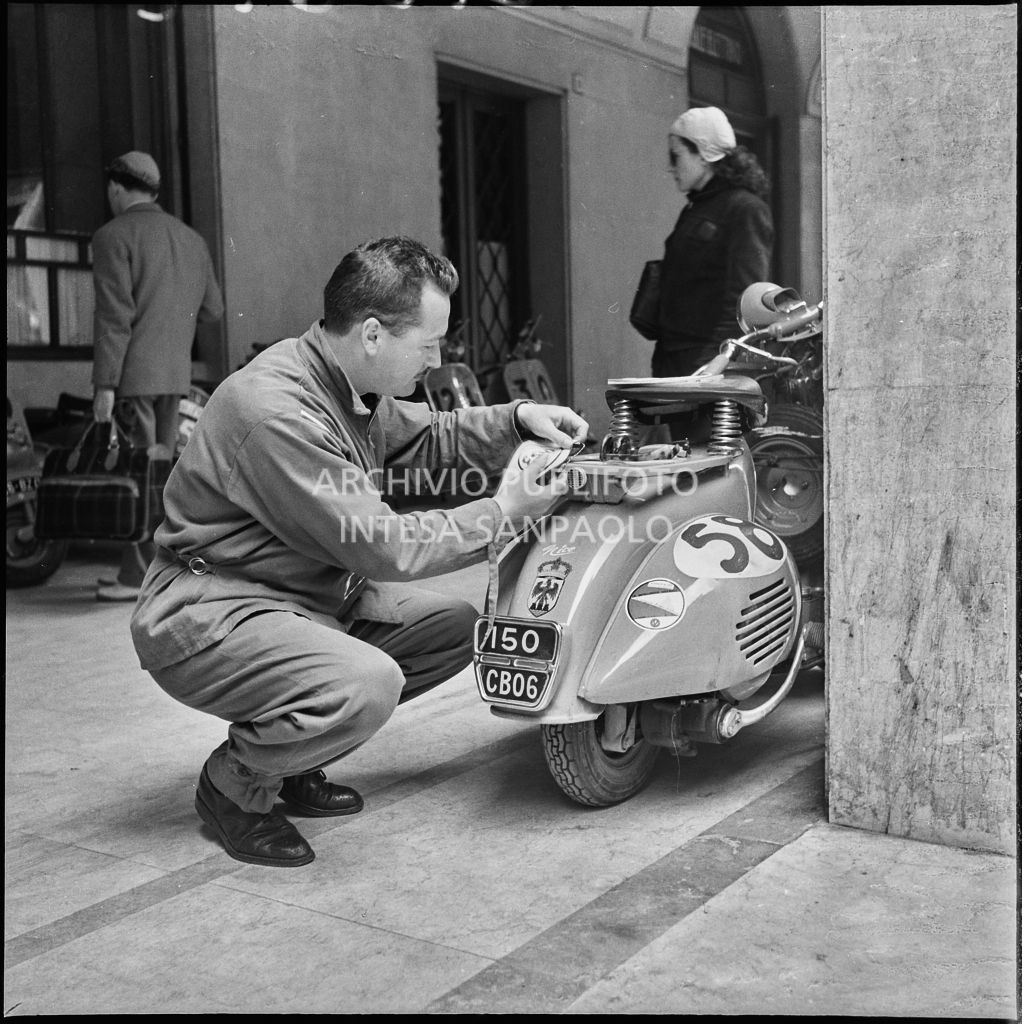 Un meccanico attacca una bandierina della Esso allo scooter di un concorrente del Vespa Club di Nizza (numero di gara 58) in occasione della competizione sportiva 1000 Km Vespistica del 1954<br>216612