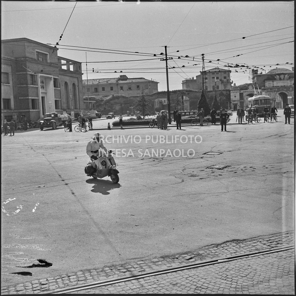 Un concorrente (numero di gara 91) sul piazzale antistante Porta Vescovo a Verona durante la competizione sportiva 1000 Km Vespistica del 1954<br>216620