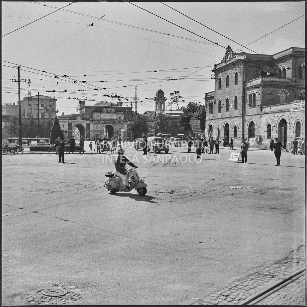 Un concorrente (numero di gara 81) sul piazzale antistante Porta Vescovo a Verona durante la competizione sportiva 1000 Km Vespistica del 1954<br>216622
