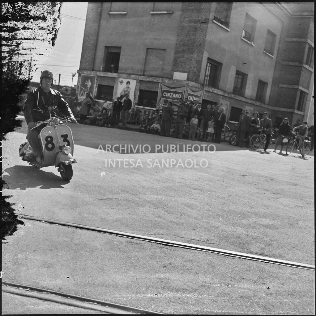 Un concorrente (numero di gara 83) sul piazzale antistante Porta Vescovo a Verona durante la competizione sportiva 1000 Km Vespistica del 1954<br>216632