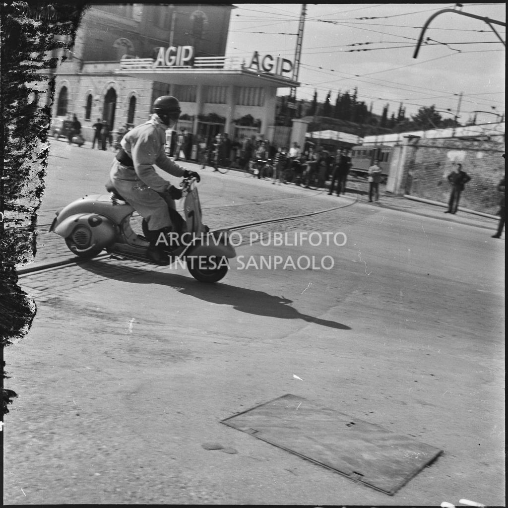 Un concorrente (numero di gara 76) sul piazzale antistante Porta Vescovo a Verona durante la competizione sportiva 1000 Km Vespistica del 1954<br>216633
