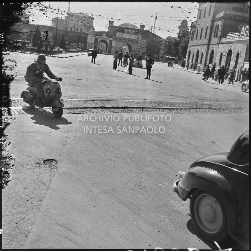 Un concorrente (numero di gara 94) sul piazzale antistante Porta Vescovo a Verona durante la competizione sportiva 1000 Km Vespistica del 1954<br>216634