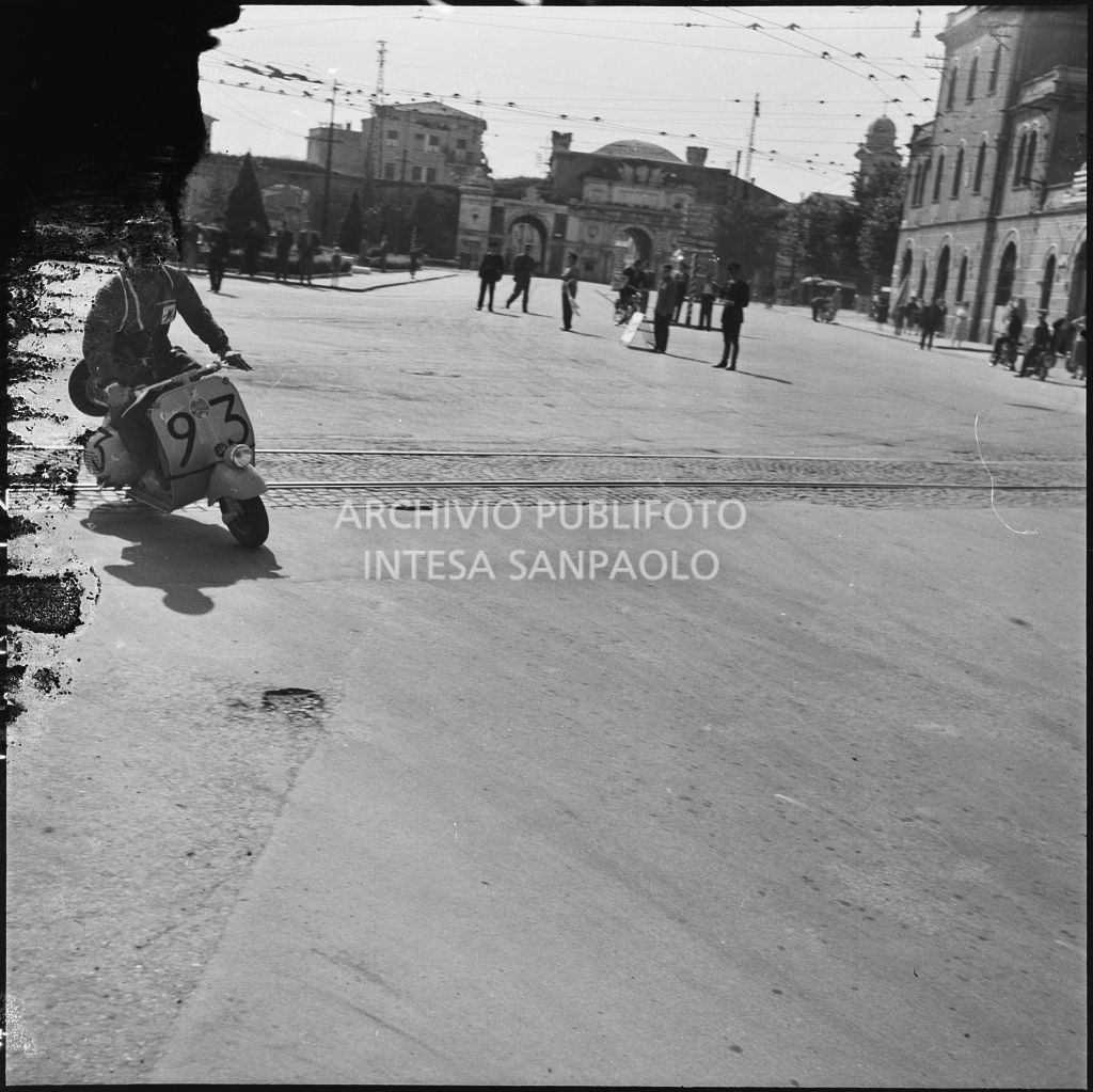 Un concorrente (numero di gara 93) sul piazzale antistante Porta Vescovo a Verona durante la competizione sportiva 1000 Km Vespistica del 1954<br>216635