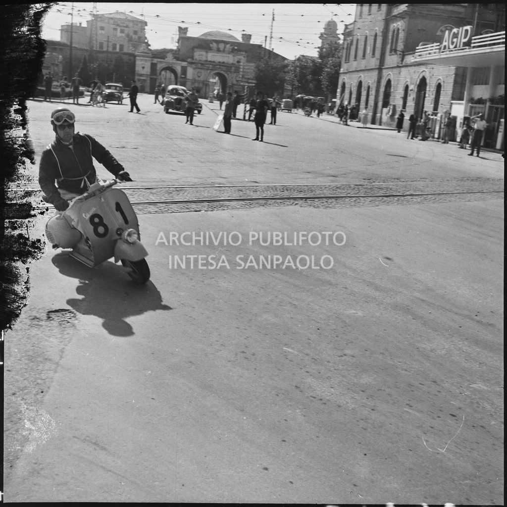 Un concorrente (numero di gara 81) sul piazzale antistante Porta Vescovo a Verona durante la competizione sportiva 1000 Km Vespistica del 1954<br>216636
