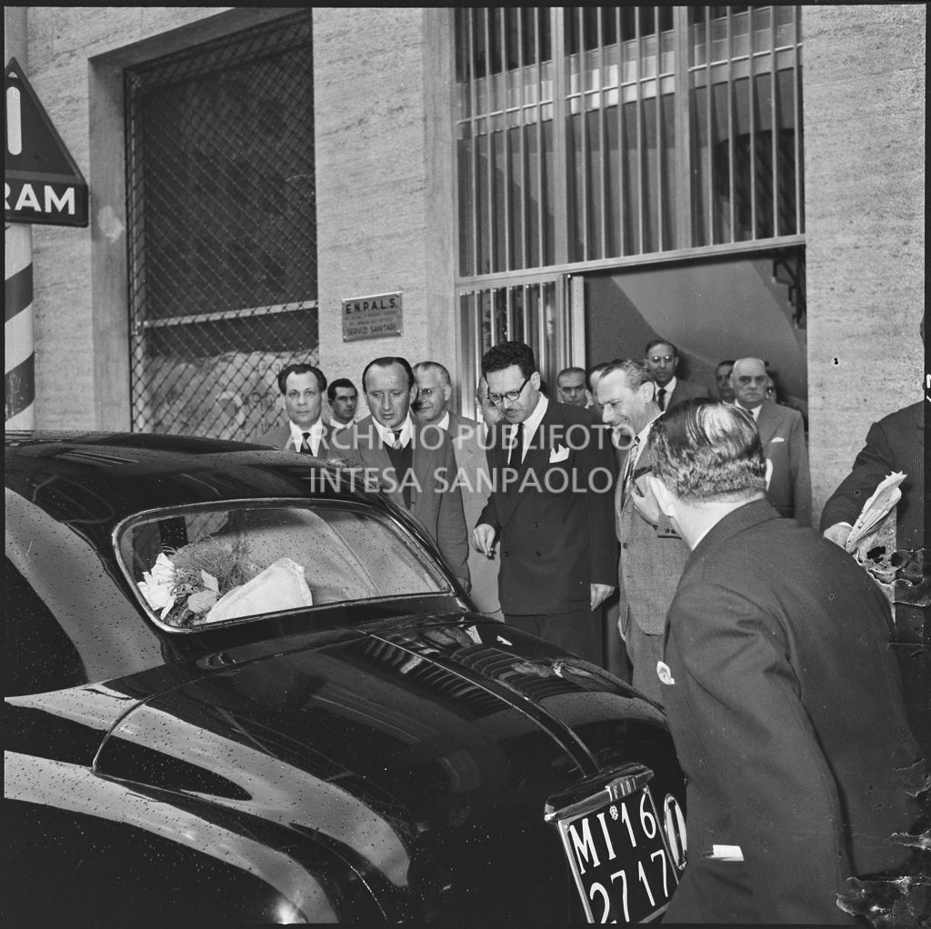 Folla intorno all'automobile dell'onorevole Ezio Vigorelli al termine dell'inaugurazione della nuova sede dell'ENPALS di Milano. Visibile sullo sfondo il prefetto di Milano Ernesto Giulio Cappa<br>216934