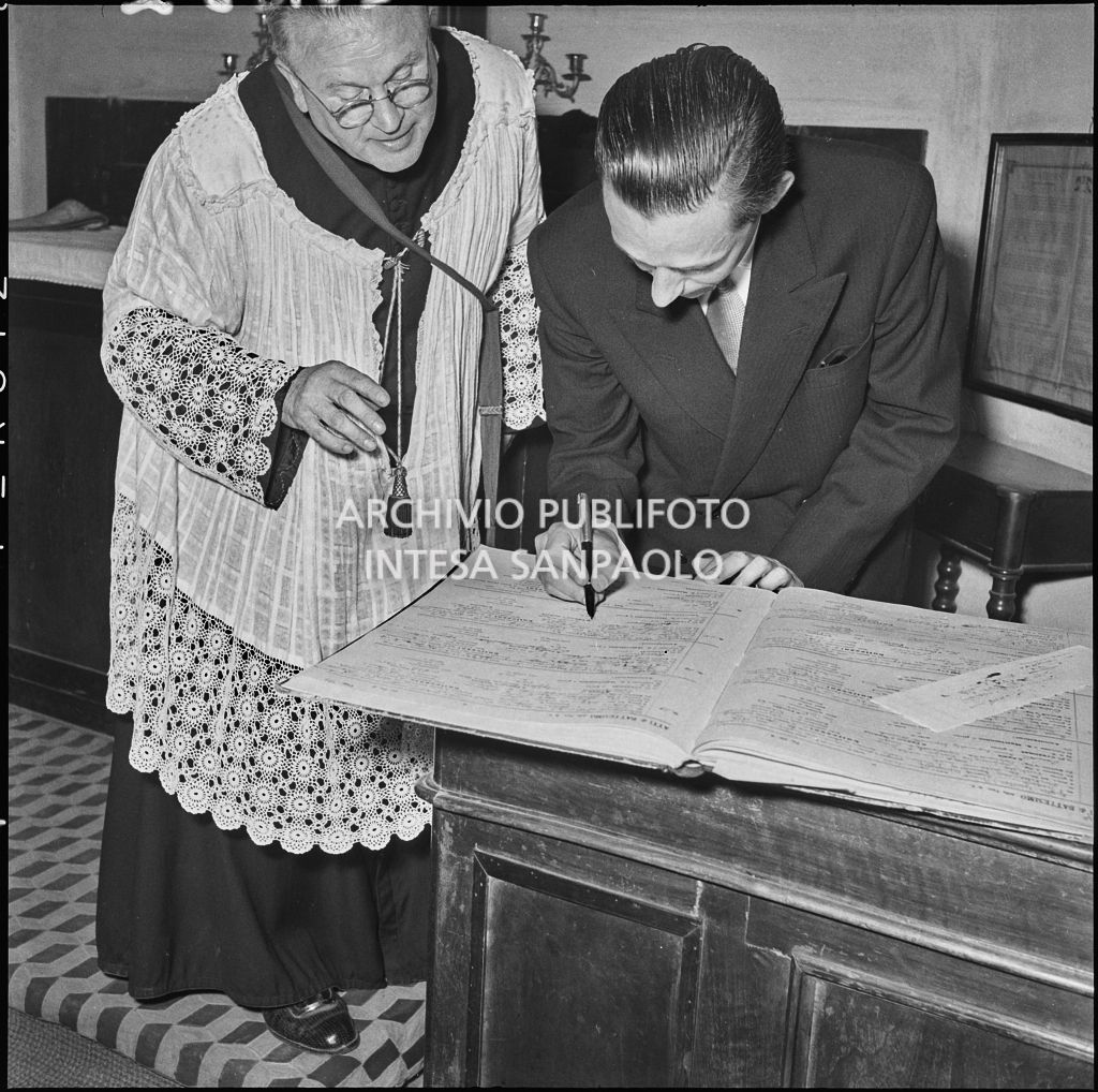 Il padrino della figlia del signor Bernardi firma il registro parrocchiale al termine del battesimo<br>221822