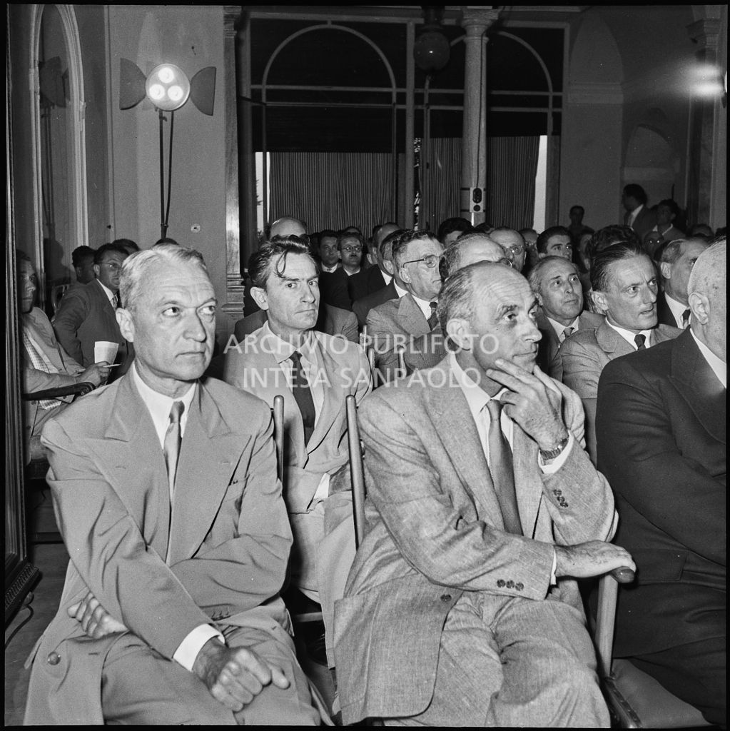 Pubblico all'inaugurazione della seconda edizione del Corso Internazionale di Fisica svoltosi a Villa Monastero a Varenna. Visibili in prima fila il professor Bernardo Rossi (primo da sinistra) e il professor Enrico Fermi (secondo da sinistra) e Eugenio Rossano (terzo da sinistra), in seconda fila il professor Gilberto Bernardini (primo da sinistra)<br>221870