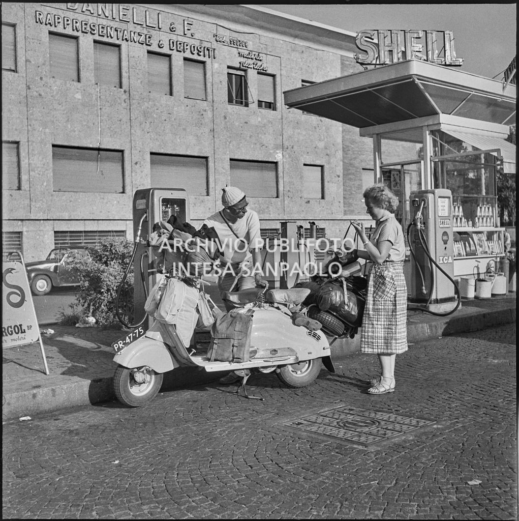 Un uomo ed una donna ad una stazione di servizio Shell con una vespa ricolma di bagagli per le vacanze estive<br>222854