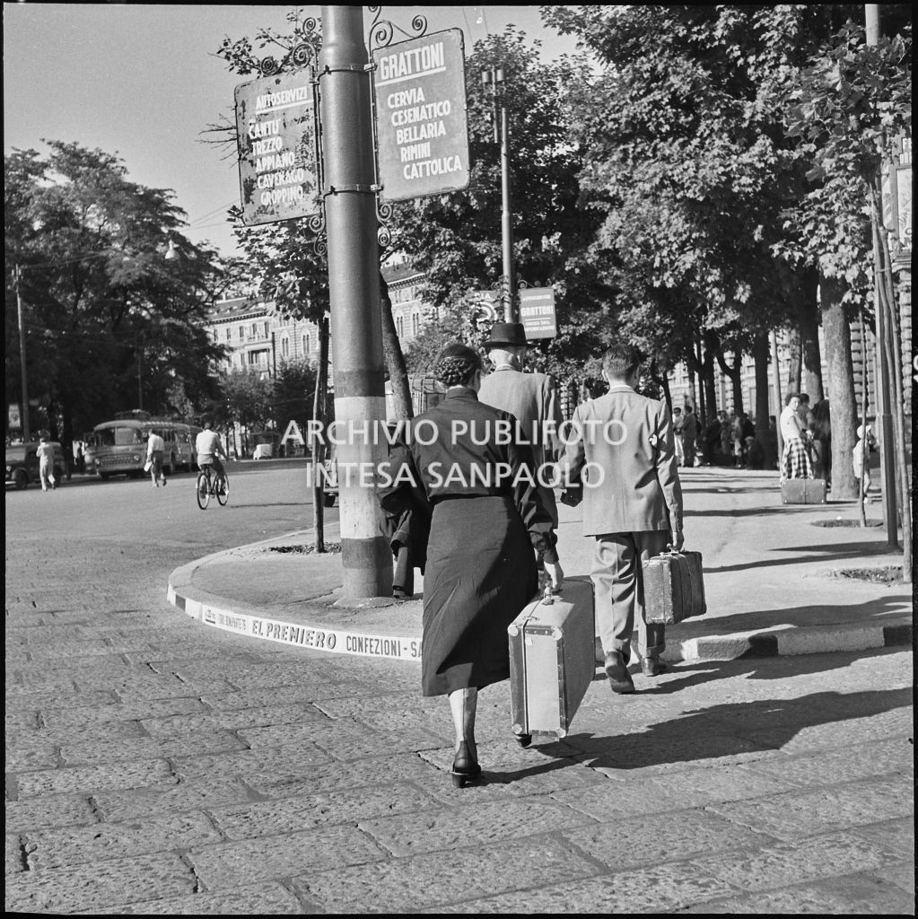 Alcuni passeggeri si dirigono con le valige alla fermata dell'autobus nei pressi del Castello Sforzesco di Milano<br>222891