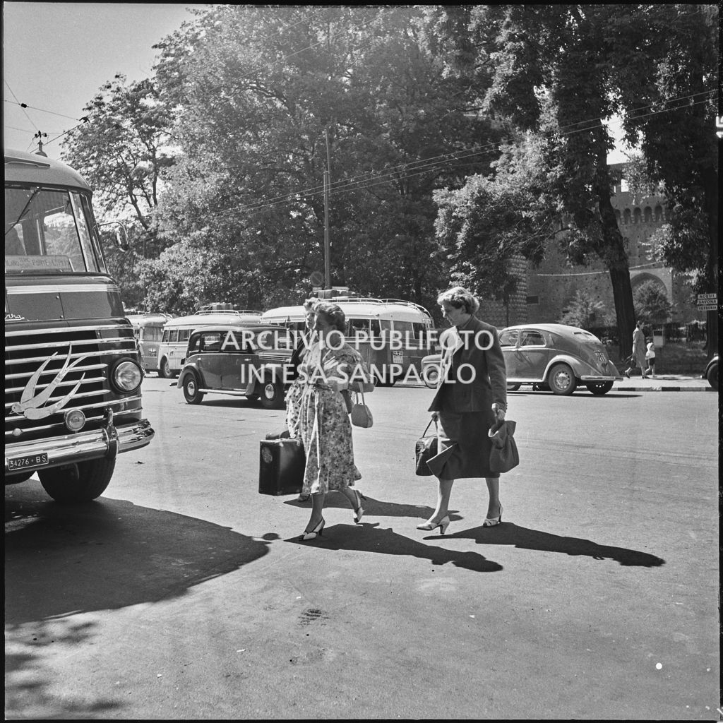 Alcuni passeggere si dirigono con le valige alla fermata dell'autobus nei pressi del Castello Sforzesco di Milano<br>222893